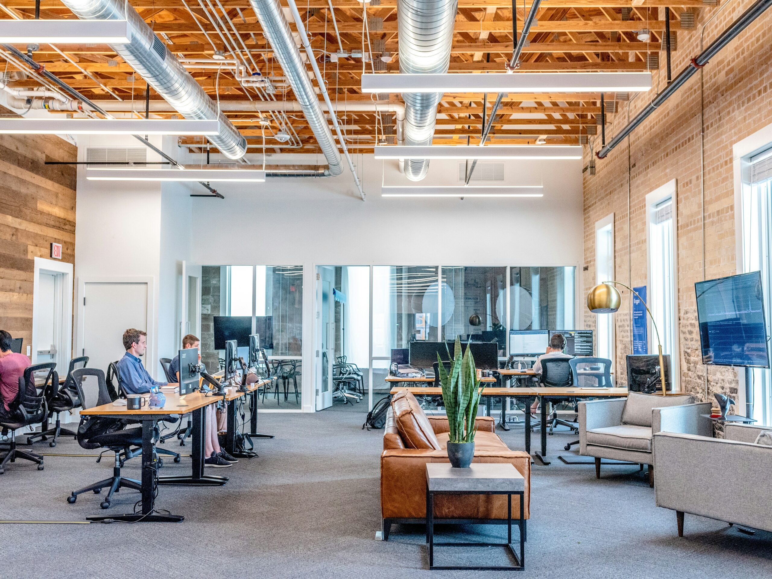 austin-distel-wawEfYdpkag-unsplash (1) a modern office with high ceilings and a couple young professionals seated and working at their desks.