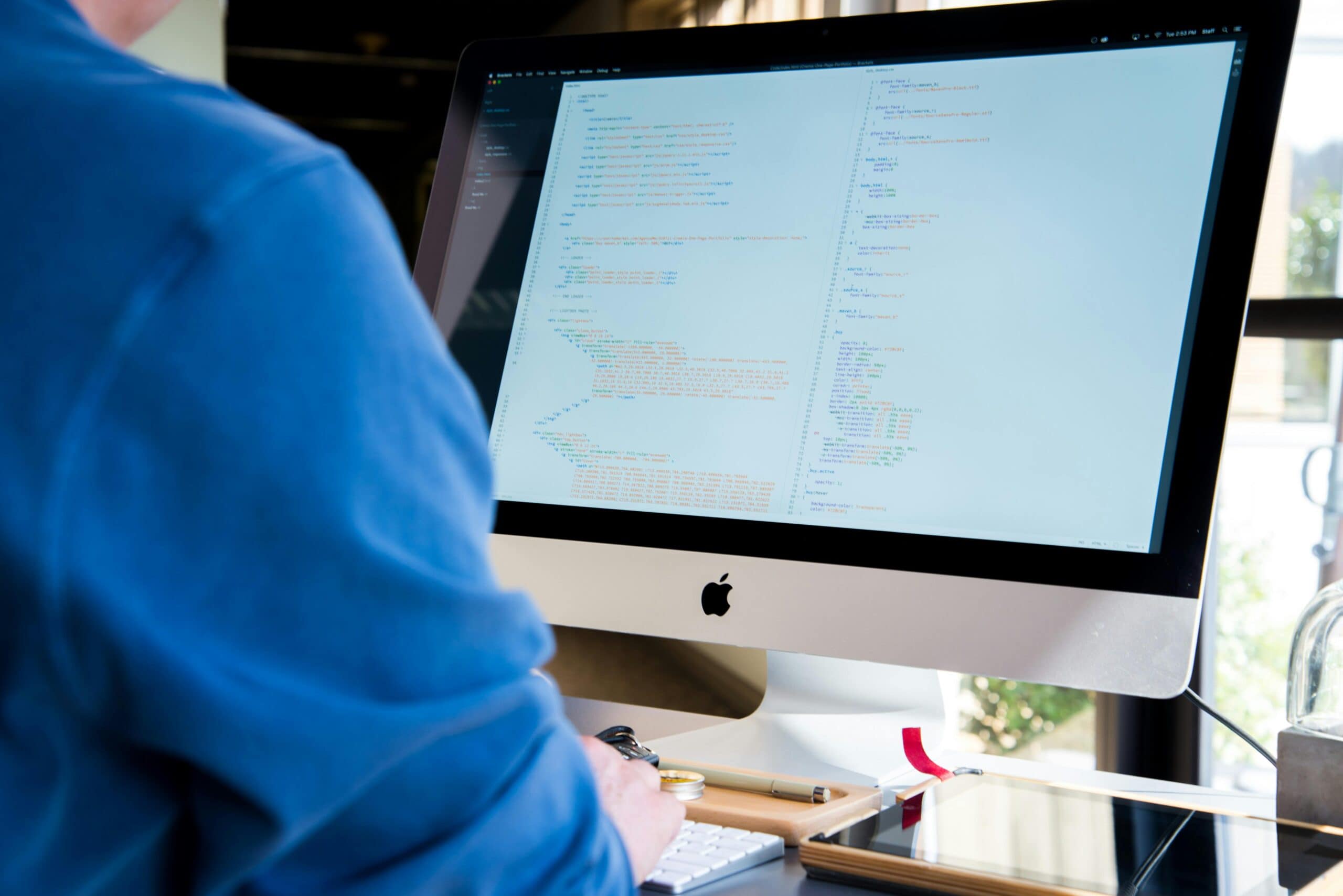 pexels-lee-campbell-18167-89724 View of the back of someone's shoulder and arm, seated at a desk working on a computer with coding on the screen.