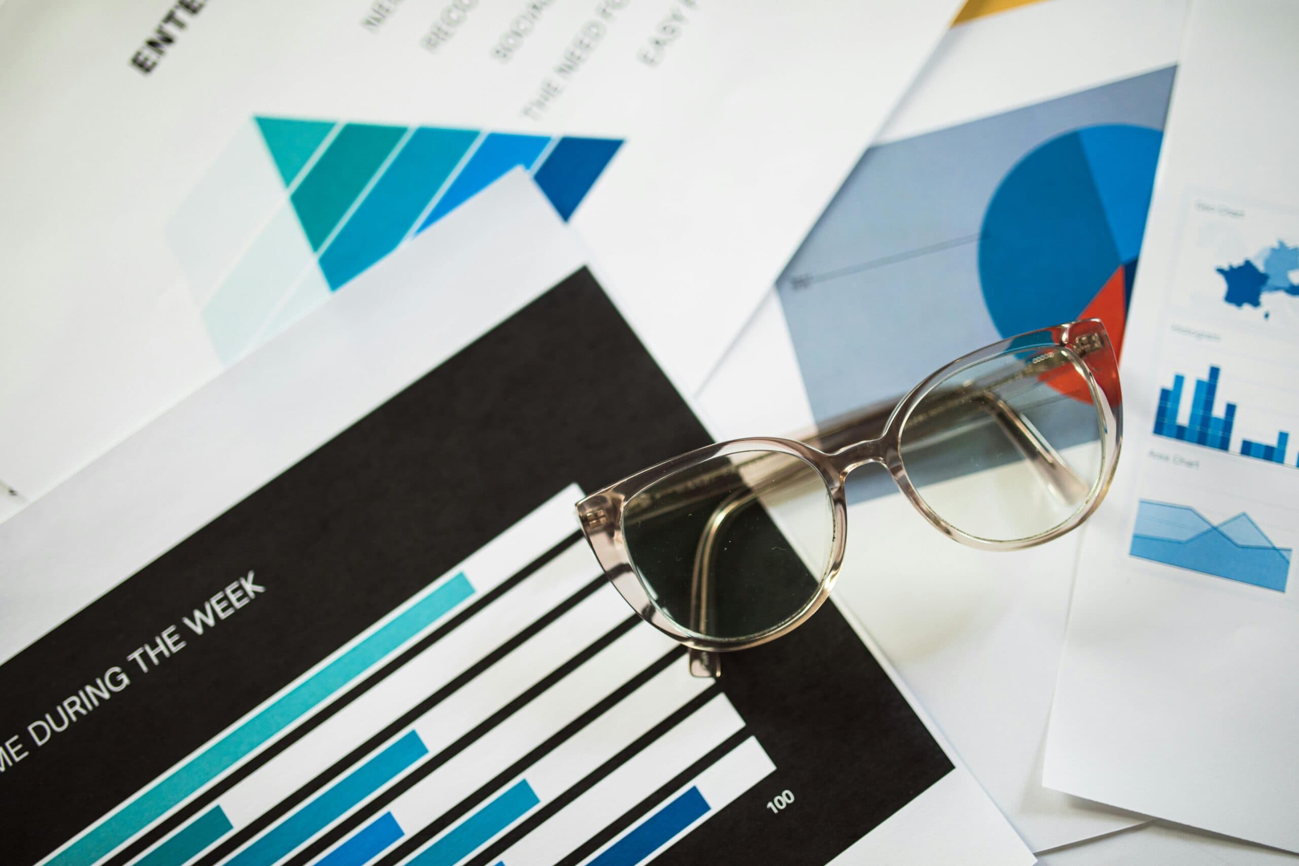 A pair of glasses on top of paperwork with graphs and charts