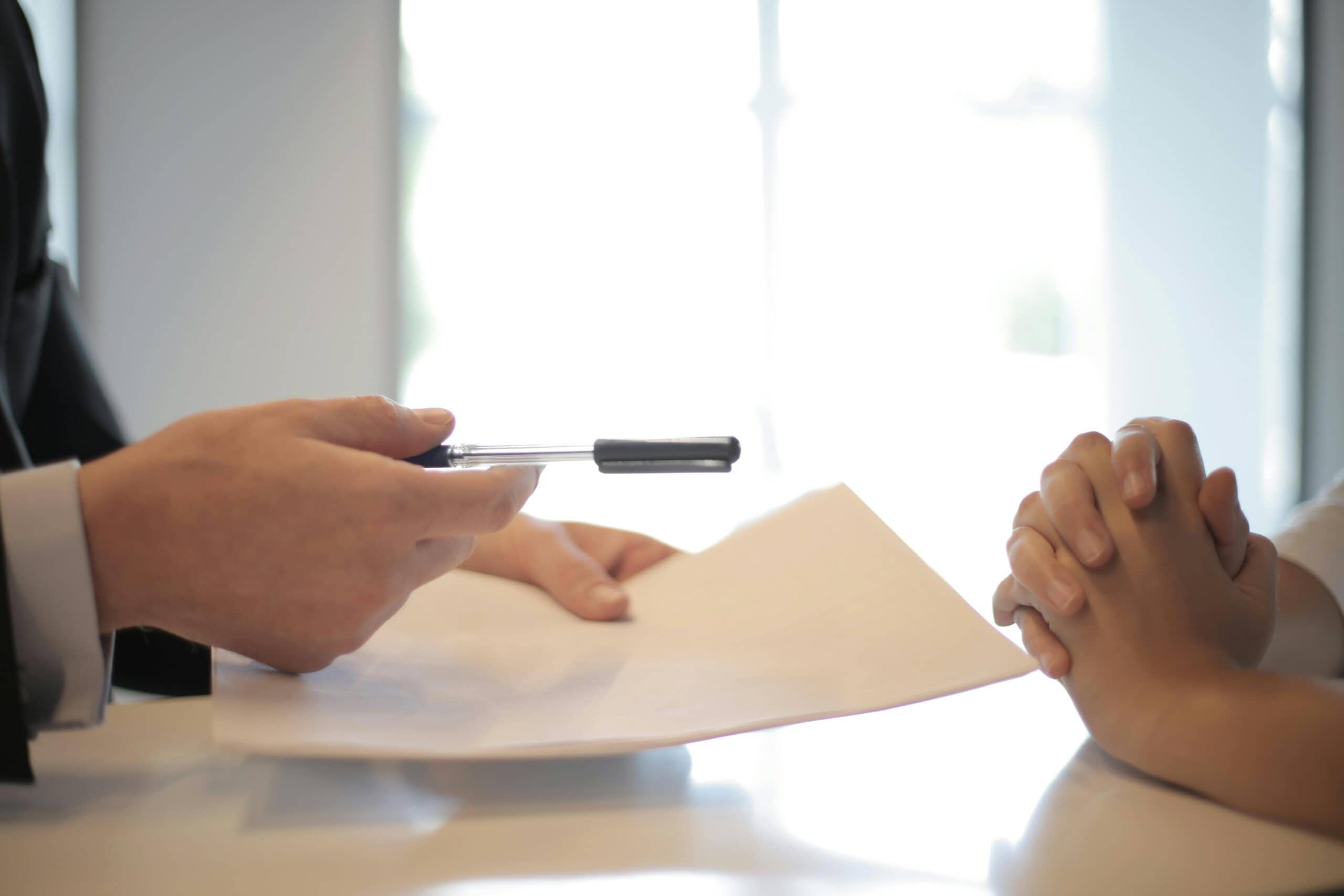 pexels-olly-3760067 (1) A business person's hands holding a pen and contract toward a set of crossed hands across from them.